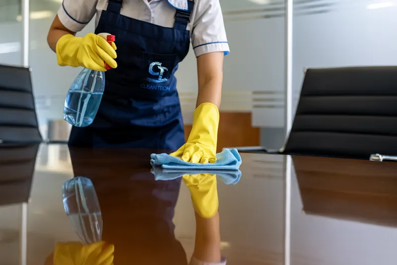 Reinigungskraft von Clean Tech wischt einen Konferenztisch im Büro